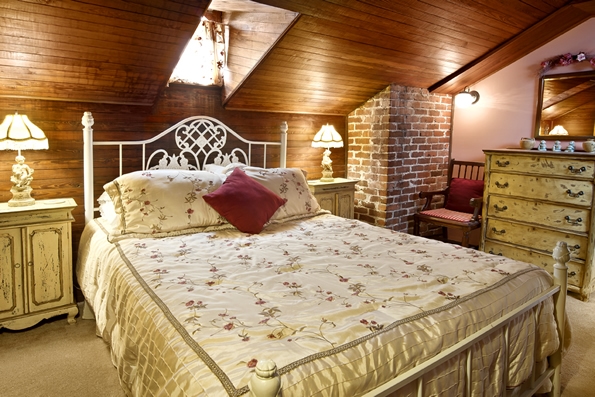 queen sized bed with pillows and nightstands with table lamps are underneath an eyebrow window above.  Dresser and sitting chair off to the side.