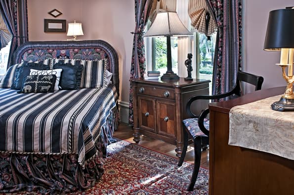 Queen sized bed with striped comforter, by the window. Antique furniture and design