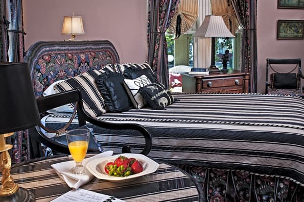 Orange juice and Strawberries on table in foreground with bed and antique furniture and window coverings in background