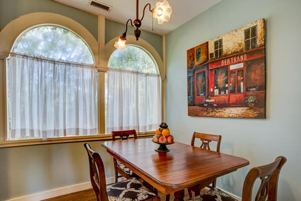 Dining area with 4 chairs and small dining table.  2 windows with sheer curtains and Art on wall behind Table