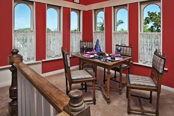 Tower area with small dining table, 4 dining chairs is setup for celebrating a birthday.  Chocolate cake and 4 placesettings on table.  tall eyebrow windows are covered with sheers on bottom half.