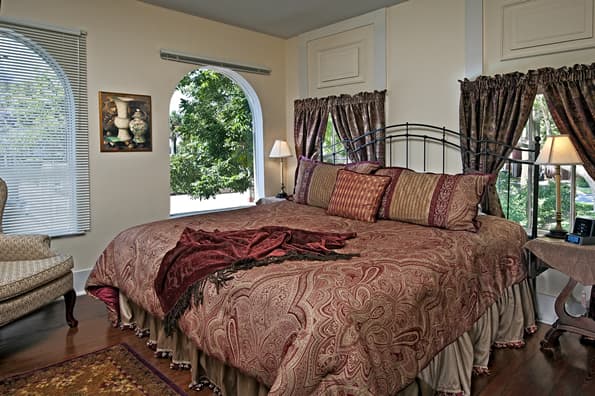 King sized bed Between curtained windows with highback sitting chair to left side