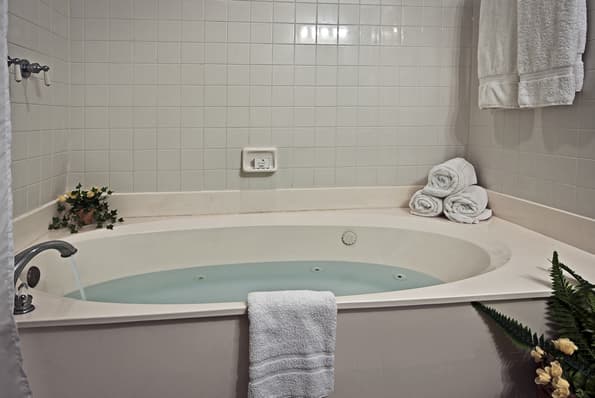 Large, jetted soaking tub with rolled and hanging towels nearby.  Roses in vase on side of tub