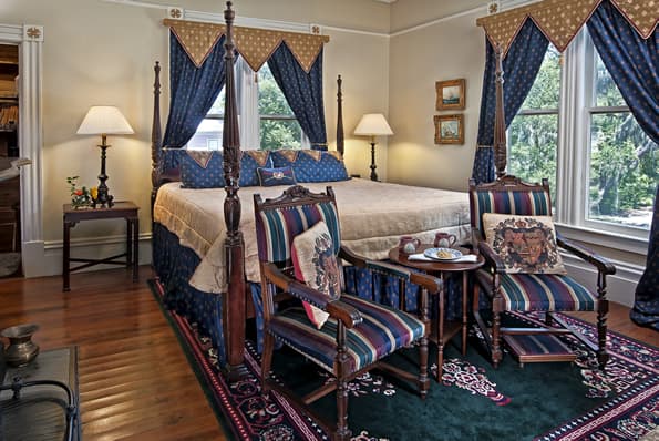 2 Highback chairs in front of King sized colonial 4 poster bed. Pillows and drapes share matching Blue and gold fabric