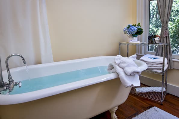 Antique Clawfoot Soaking tub, with wraparound shower curtain. Flowers and towels on small table near Tub