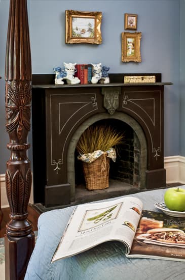 Carved Soapstone fireplace with paintings on walls over mantle. Colonial 4 poster bed in foreground.