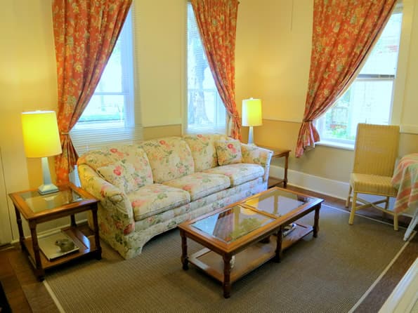 Floral sofa in yellow living room with contrasting floral curtains on windows.  two end tables and lamps are to the side of the sofa.  Coffee table in front of sofa.
