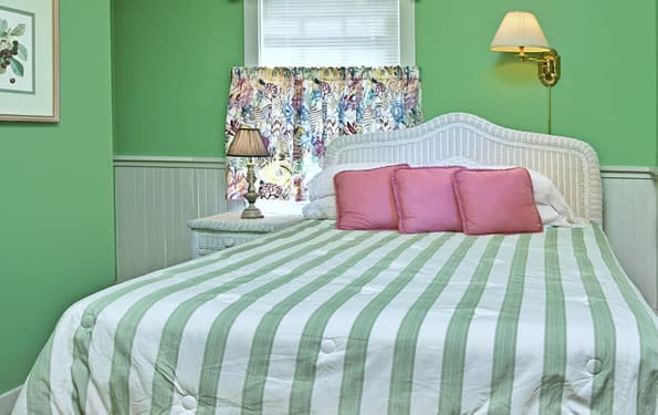 Queen sized bed with wicker headboard. wicker nightstand and table lamp to the side.