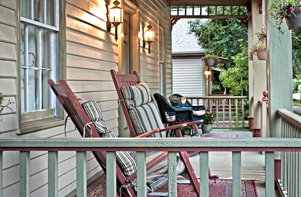 Side view of front porch with rocking chairs in foreground and chairs and table in background.