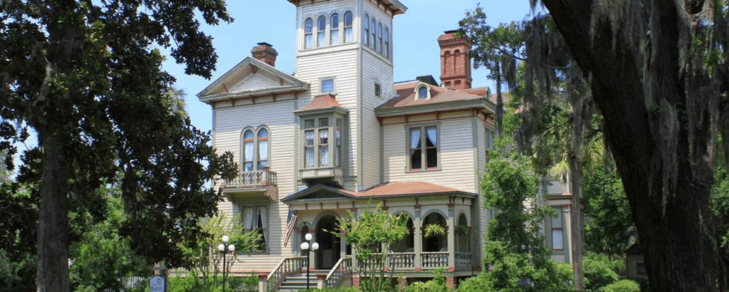 A Victorian-style house surrounded by lush greenery.