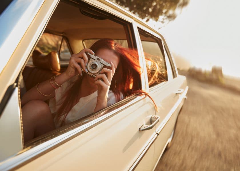 A woman with long red hair takes a photo from a car window while driving on a scenic road. A woman with long red hair takes a photo from a car window while driving on a scenic road.