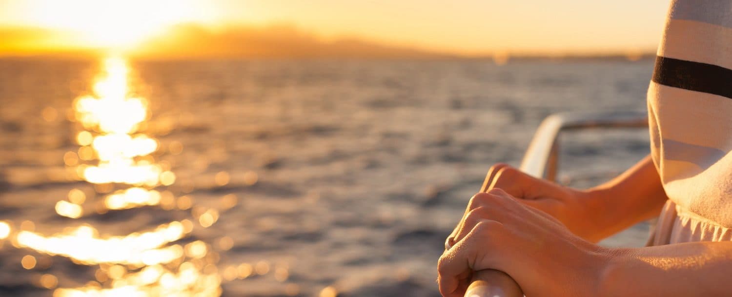 A person's hands resting on a railing with a sunset reflecting on the water.
