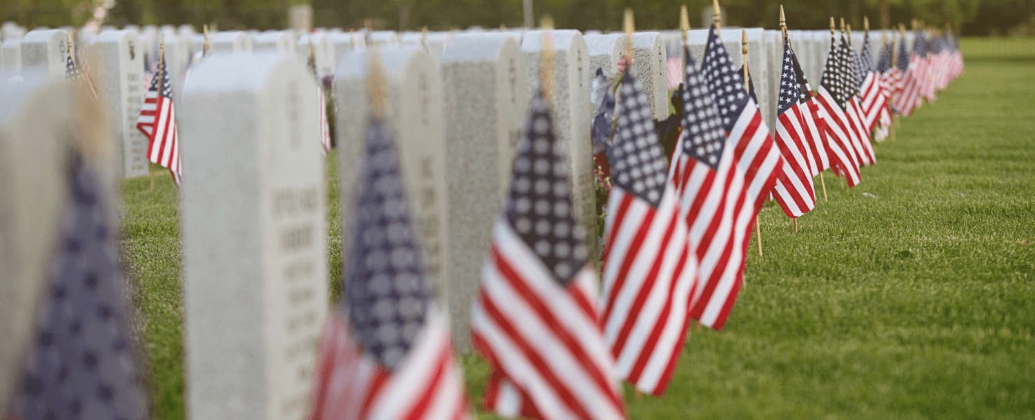 A row of gravestones adorned with small American flags in a grassy cemetery.