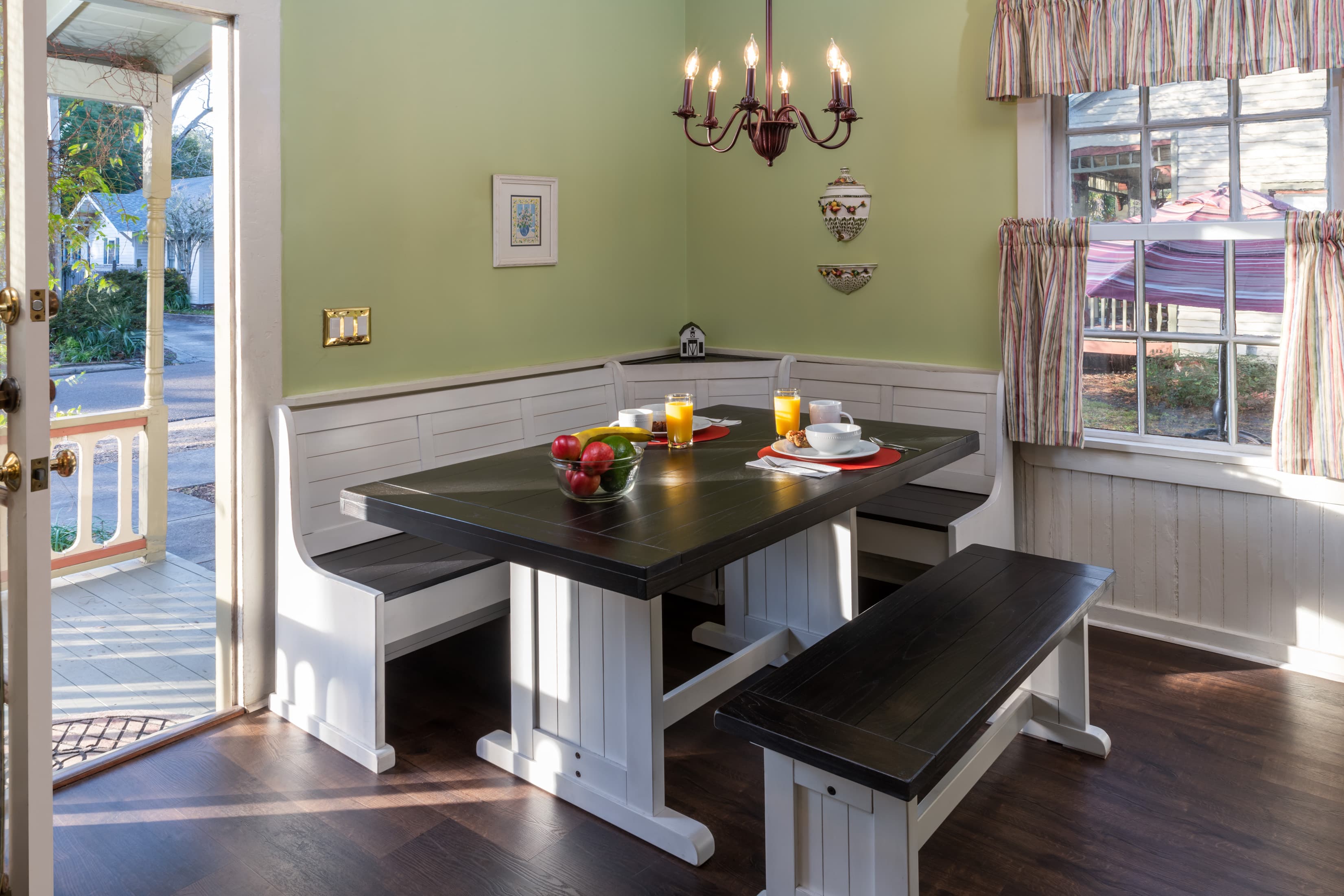 Inviting dining nook with built-in bench seating, farmhouse table, hardwood floors, and natural sunlight streaming through cottage windows.