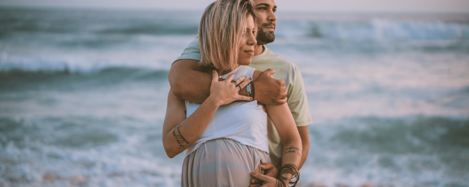 A couple embraces on the beach, with the ocean waves in the background.