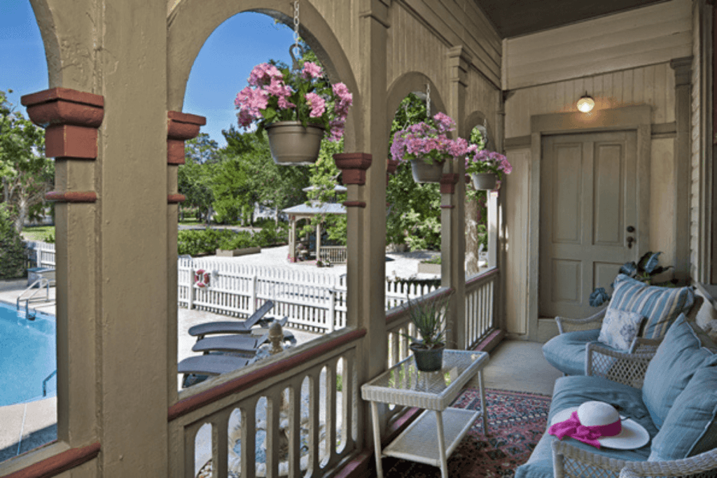 A cozy porch with potted flowers, a comfortable seating area, and a view of the pool and garden.