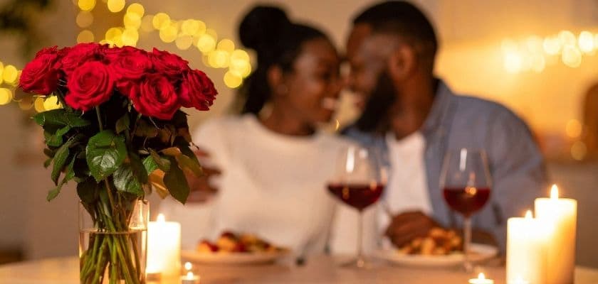 A romantic dinner setting with a couple embracing, surrounded by roses and candlelight.