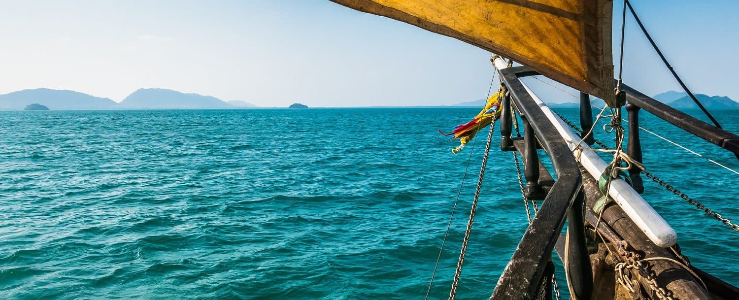 A boat's bow cutting through turquoise waters with distant islands on the horizon.