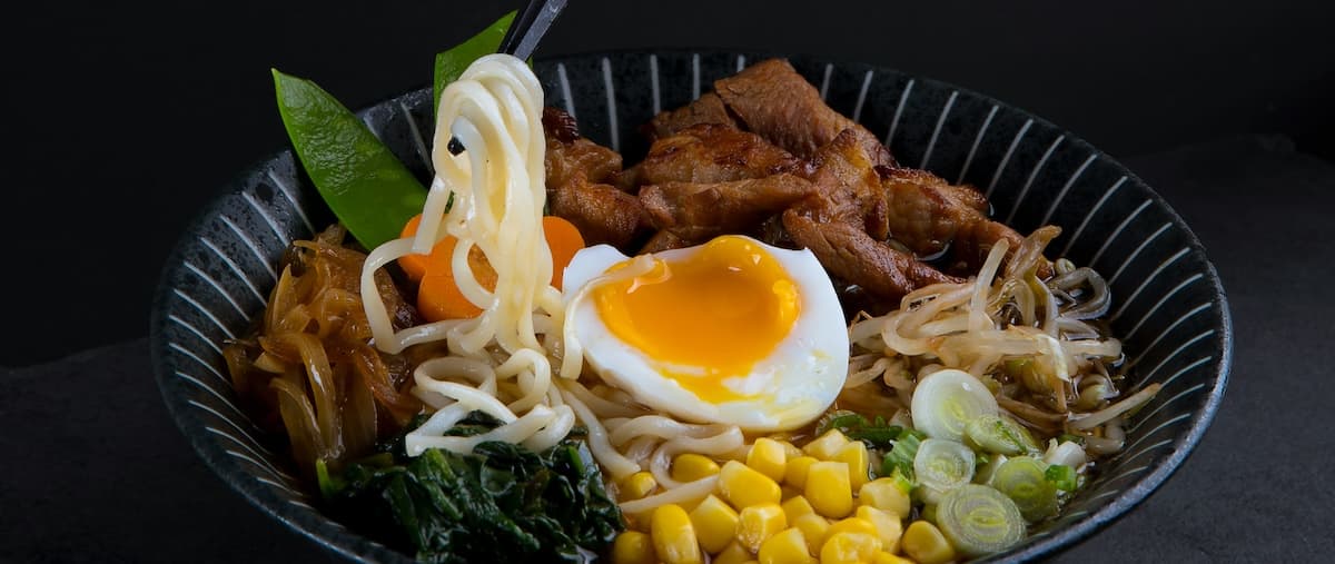 A bowl of ramen topped with a poached egg, sliced meat, vegetables, and noodles.