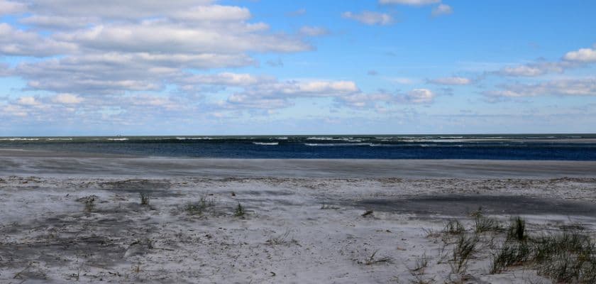 A serene beach scene with waves and scattered clouds in a blue sky.