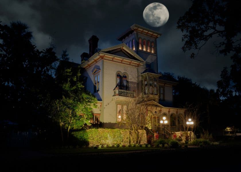 A historic Victorian house illuminated at night under a bright full moon.