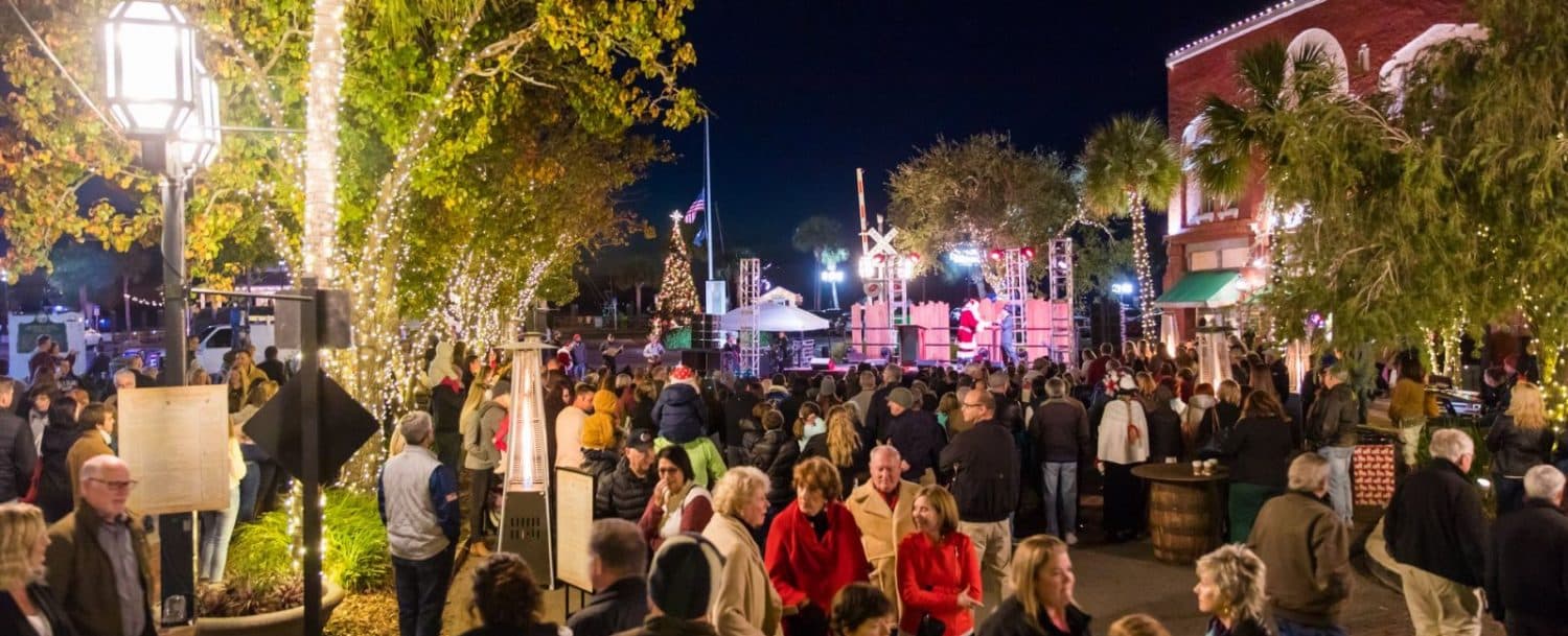 A large crowd gathers at night to enjoy a festive outdoor event with decorations and lights.