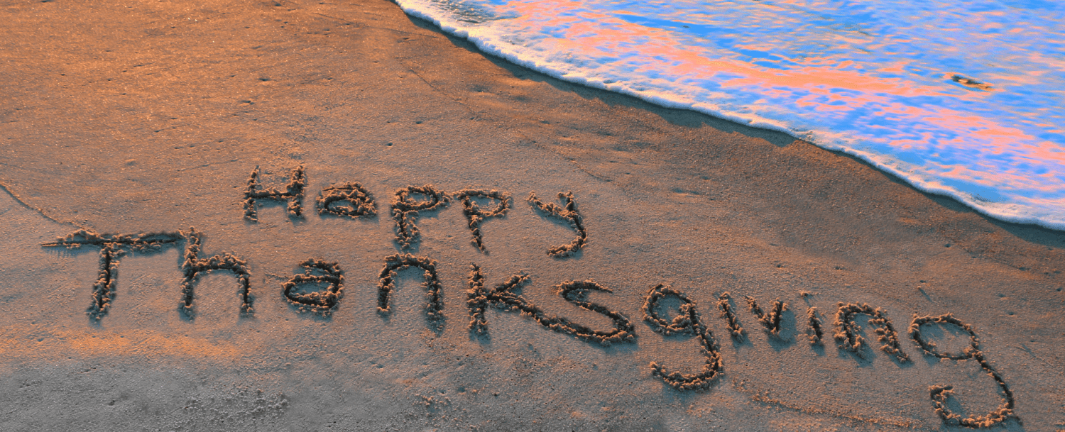 The phrase "Happy Thanksgiving" is written in sand near the ocean.