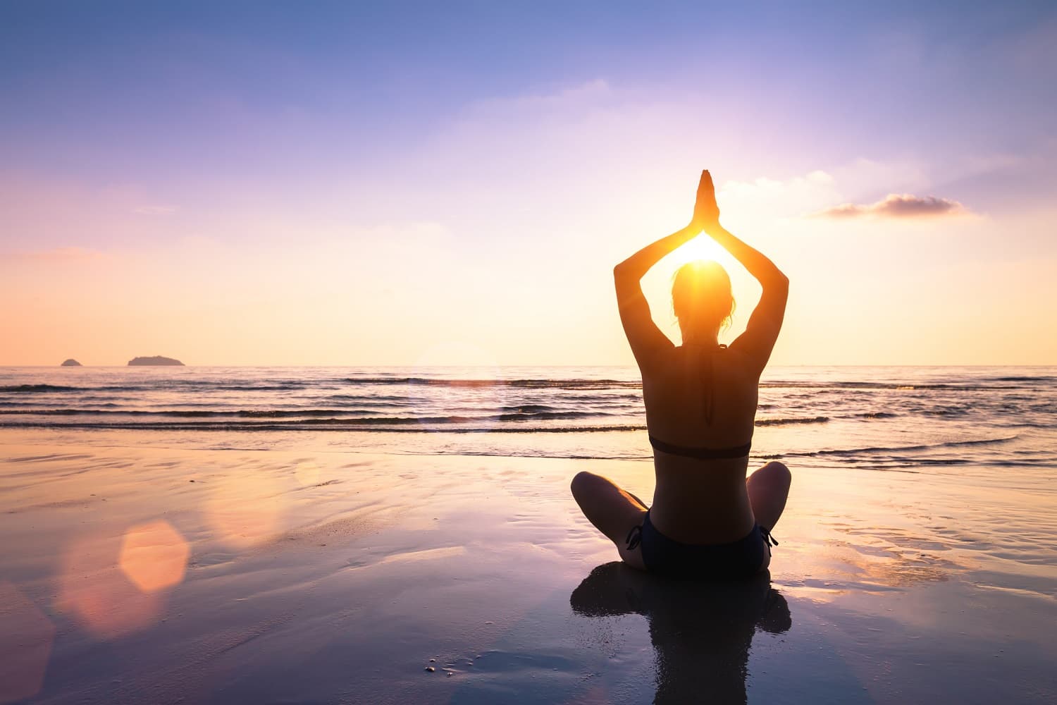 A person is practicing yoga at sunset on a beach.