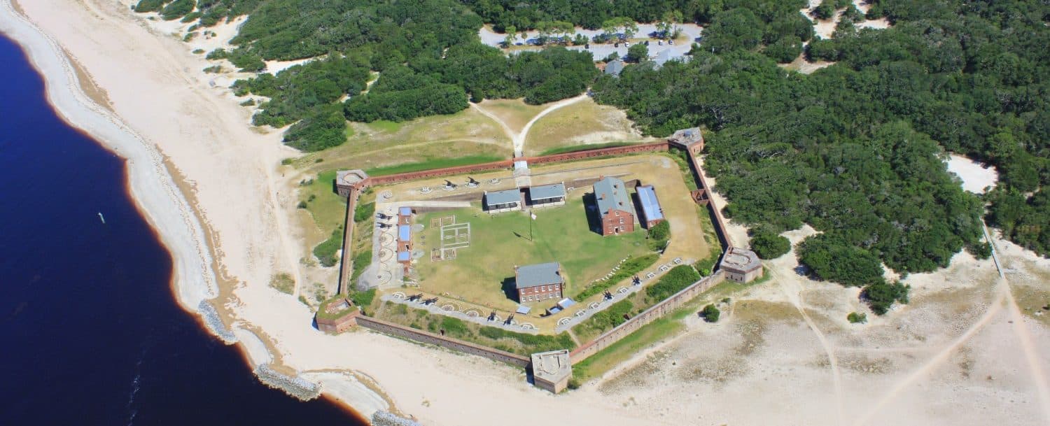 Aerial view of a historic fort surrounded by sandy beach and greenery.