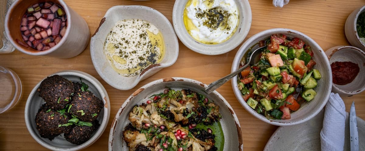 A spread of Middle Eastern dishes, including falafel, salad, yogurt, and a drink, arranged on a wooden table.