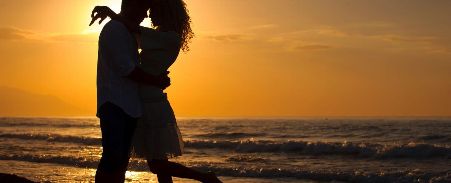 Silhouetted couple sharing a romantic kiss at sunset near the ocean.