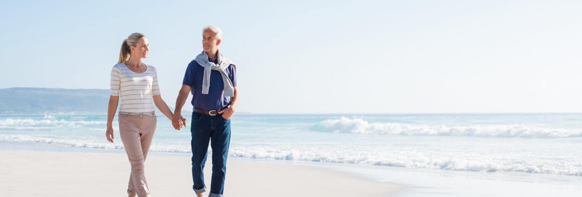 A couple walks hand-in-hand along a serene beach with gentle waves.
