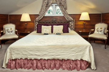 A cozy bedroom featuring a large bed with a decorative quilt, flanked by two elegant chairs and lamps.