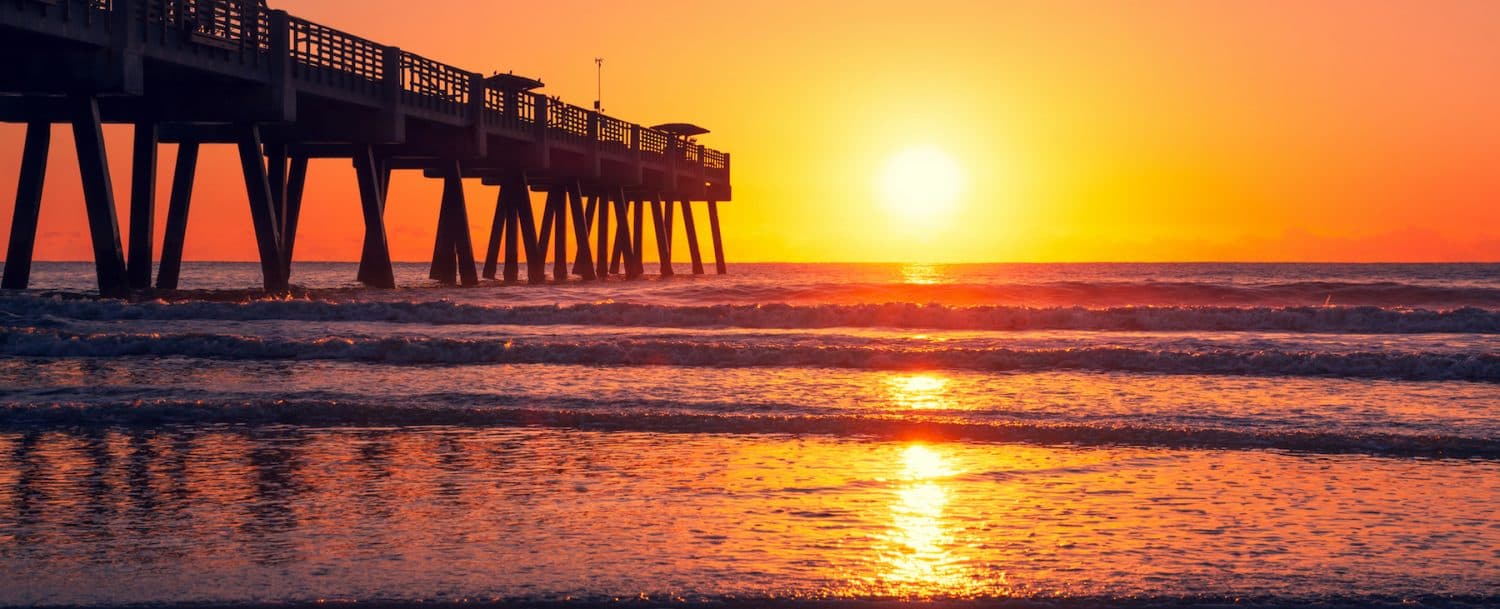Sunrise over a pier with golden light reflecting on the ocean waves.