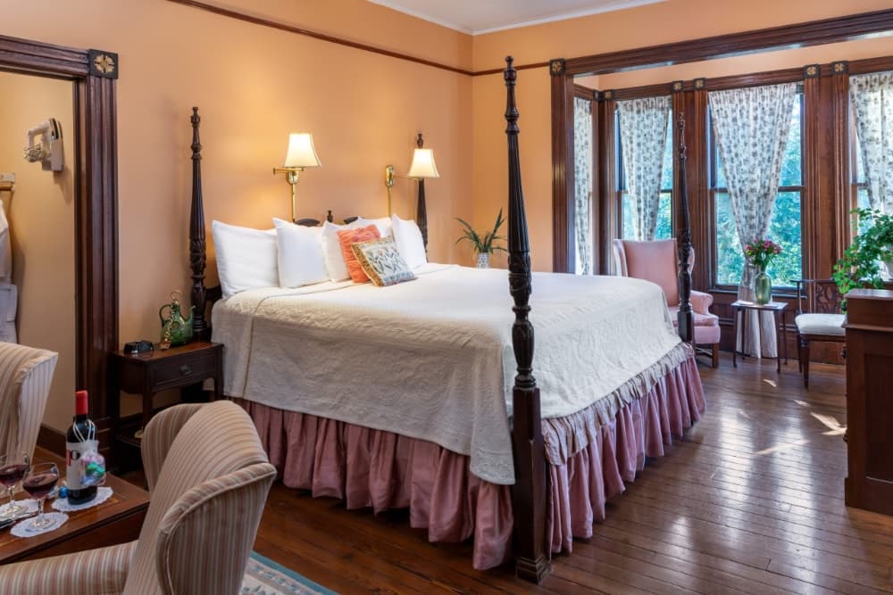 Cozy bedroom featuring a four-poster bed, elegant seating, and large windows with floral curtains.