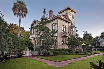A large Victorian-style house surrounded by greenery and a manicured lawn.
