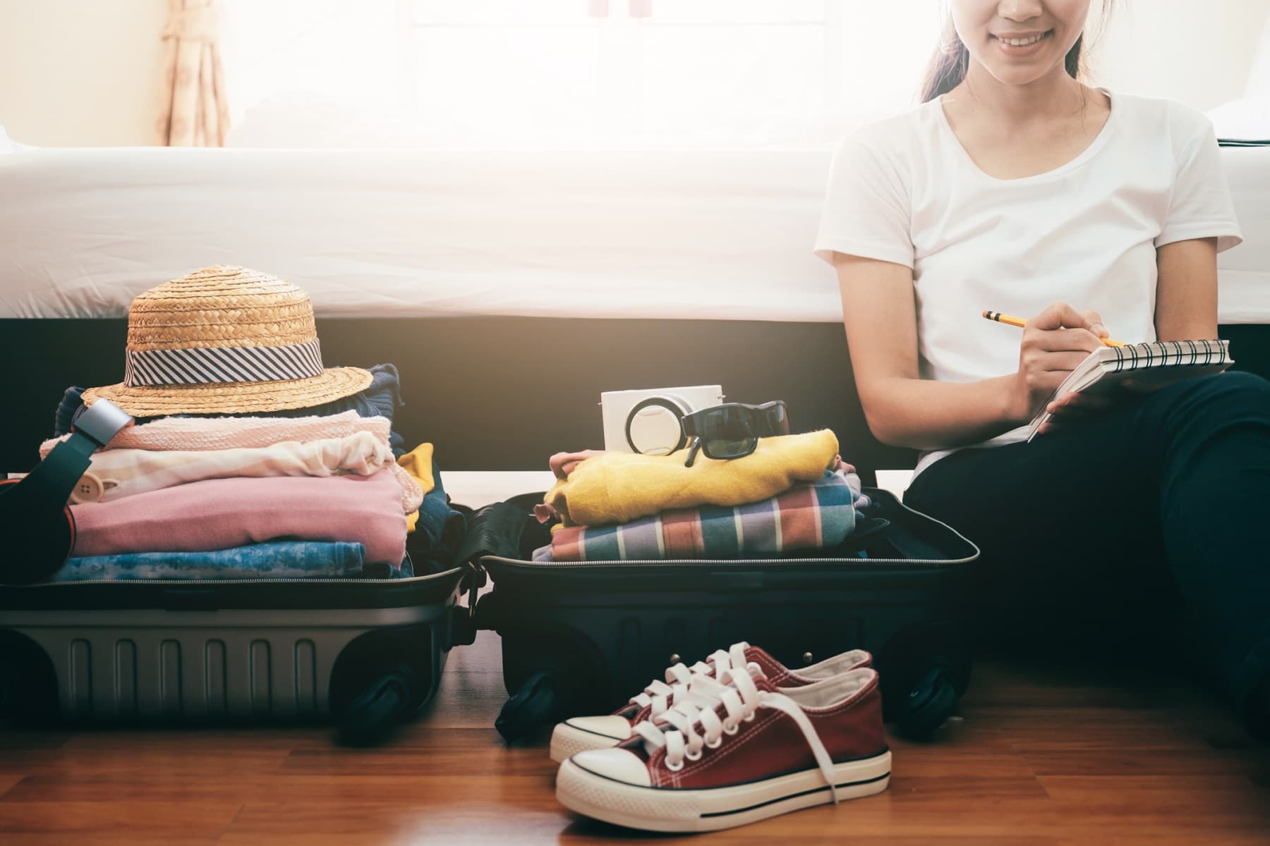 A person sits on the floor next to two packed suitcases, writing in a notebook beside a pair of sneakers. A person sits on the floor next to two packed suitcases, writing in a notebook beside a pair of sneakers.