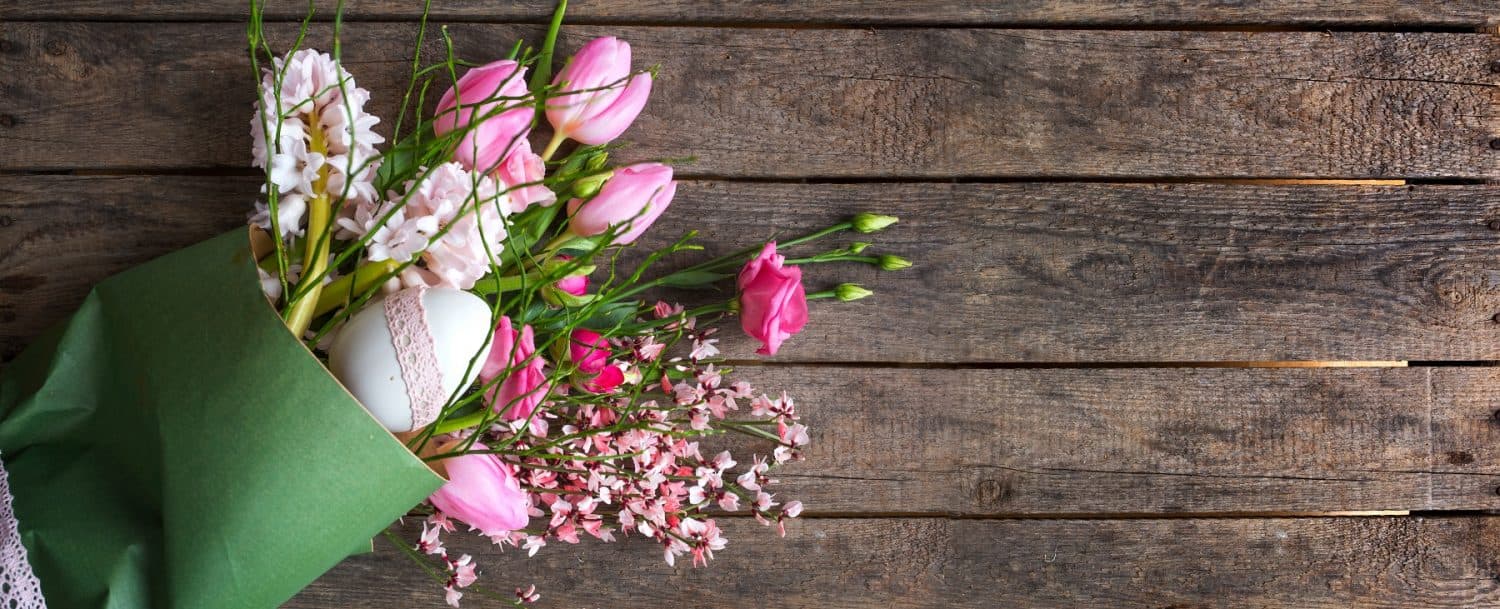 A bouquet of pink tulips and delicate flowers with a decorated egg, arranged on a wooden surface.