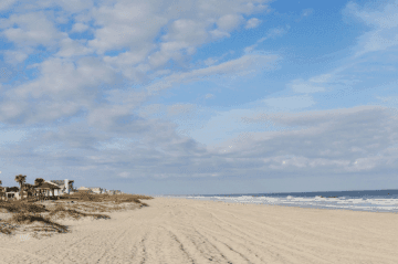 A serene beach with soft sand, gentle waves, and a partly cloudy sky.