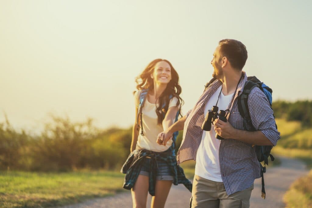 A happy couple walks hand-in-hand along a sunlit path, surrounded by nature.