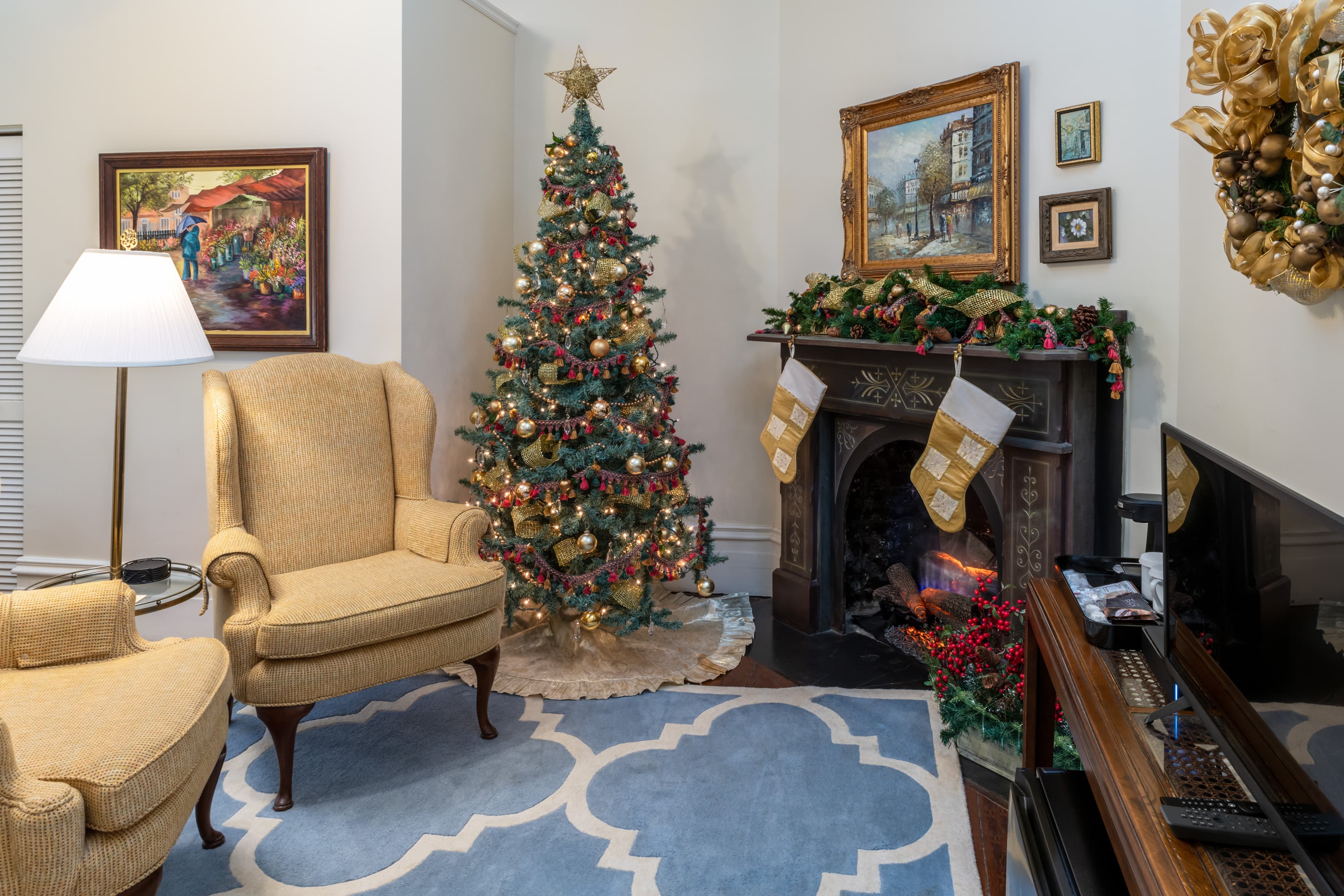Festively decorated guest suite showcasing a Christmas tree, holiday garland and stockings on a decorative fireplace, comfortable seating, hardwood floors, and elegant seasonal décor.