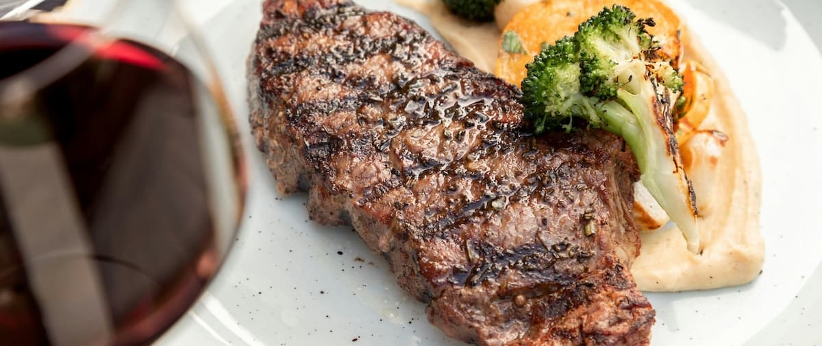 A grilled steak served with creamy mashed potatoes and broccoli, accompanied by a glass of red wine.