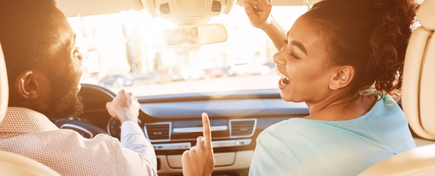 A man and woman are joyfully singing and laughing while sitting in a car.