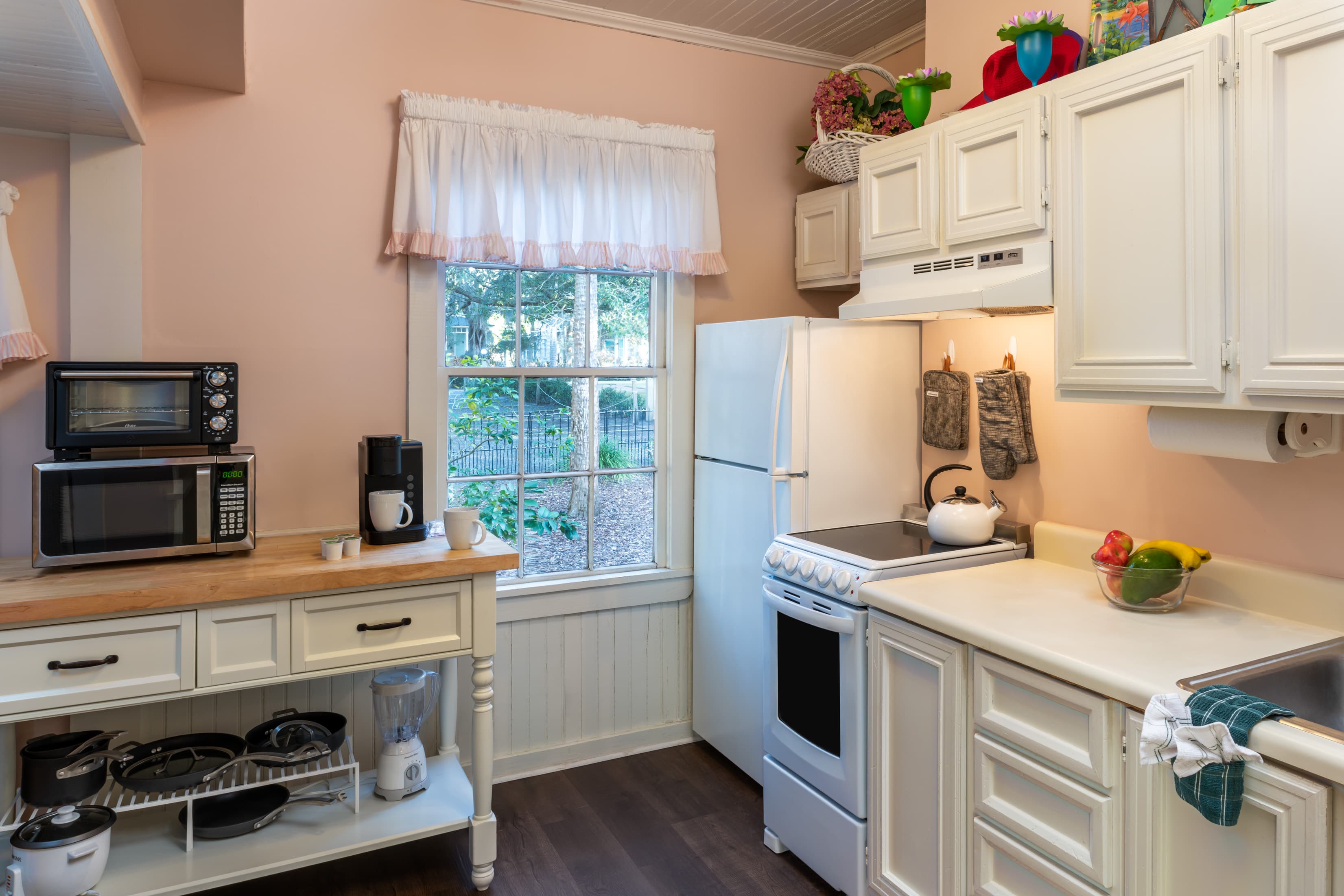 Charming cottage kitchen with full-size refrigerator, stove, microwave, coffee station, farmhouse cabinetry, and sunlit window views.