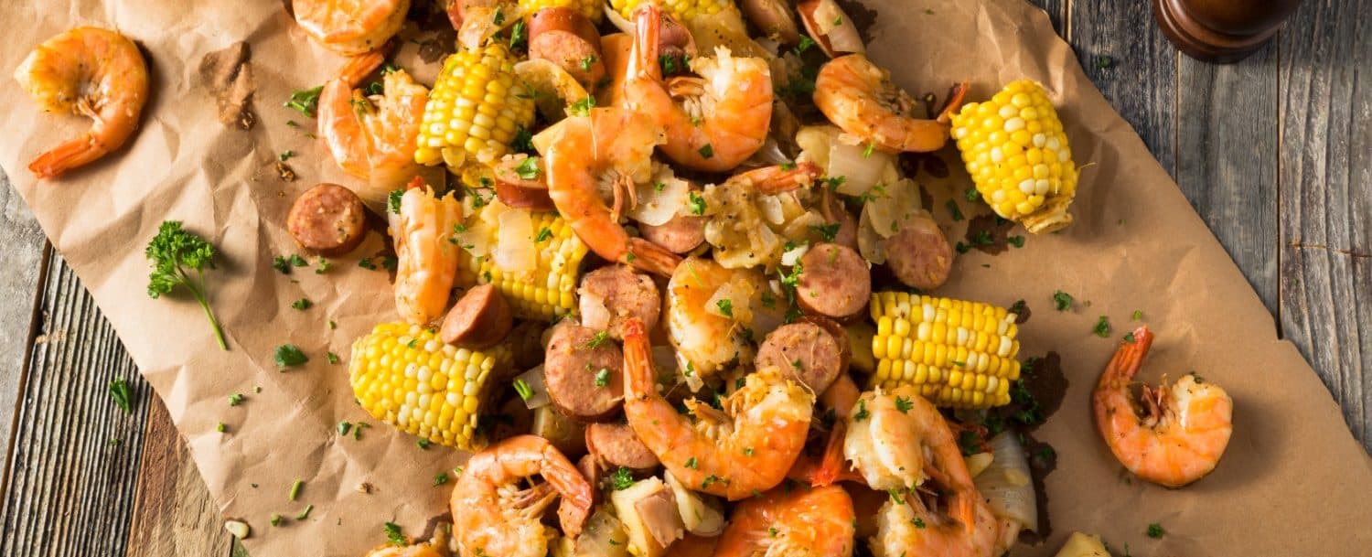 A pile of shrimp, corn, sausage, and seasoning on brown paper.