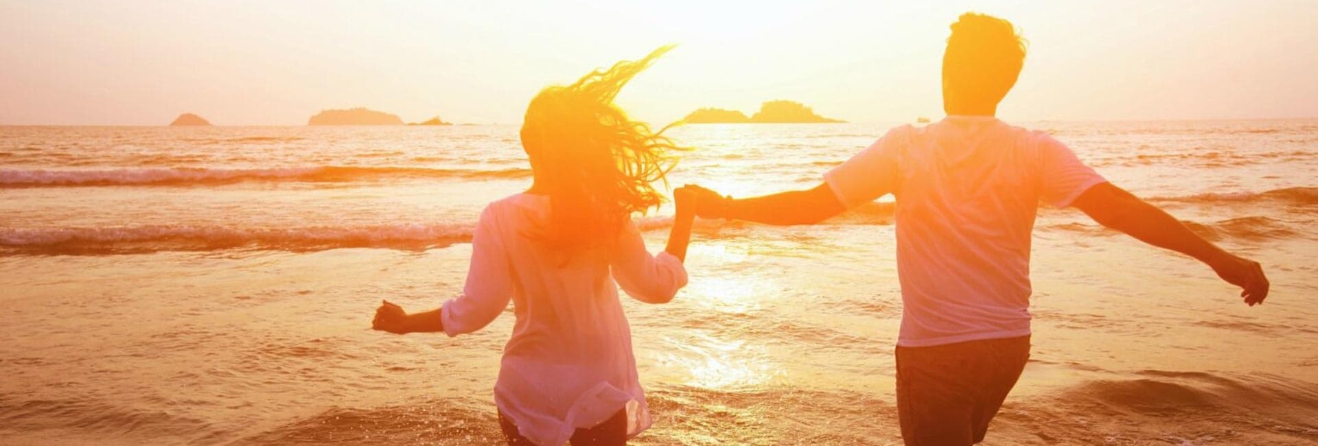 A couple runs hand in hand along a beach at sunset.