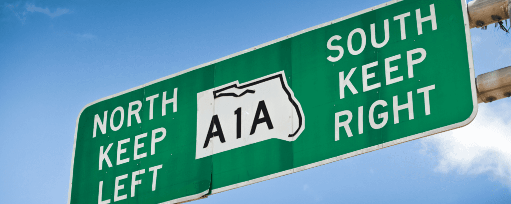 Green highway sign displaying directions for North and South, indicating to keep left for North and right for South on A1A.