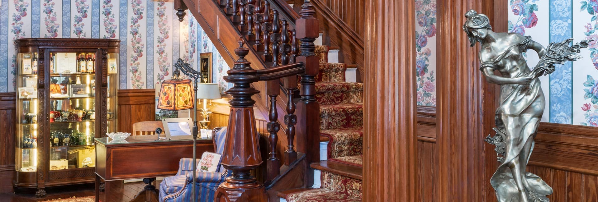 A warmly decorated foyer featuring a staircase, antique furnishings, and a decorative statue.