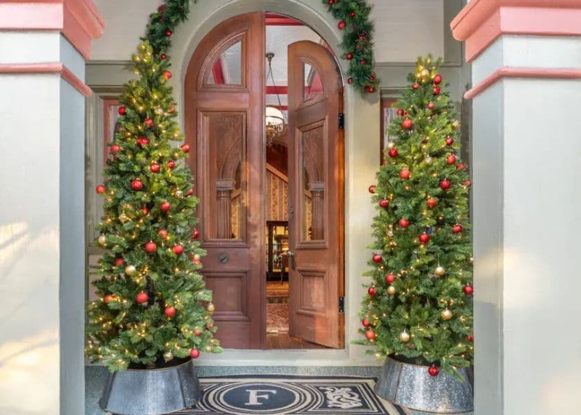 A beautifully decorated entrance with two Christmas trees flanking a double wooden door.
