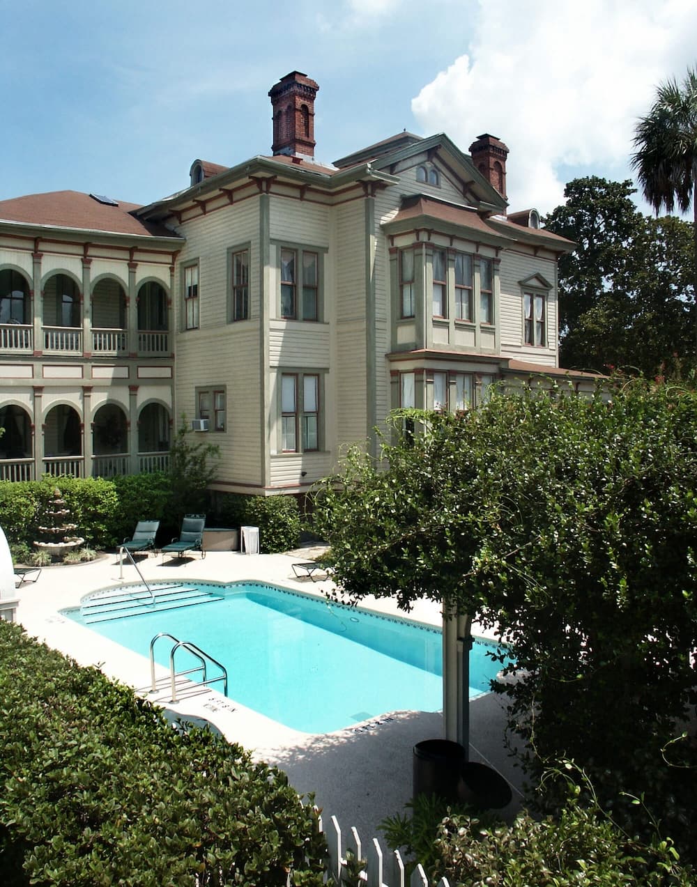 A Victorian-style mansion with a swimming pool surrounded by lush greenery.